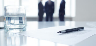 Image of business document, pen and glass of water at workplace with group of colleagues on background