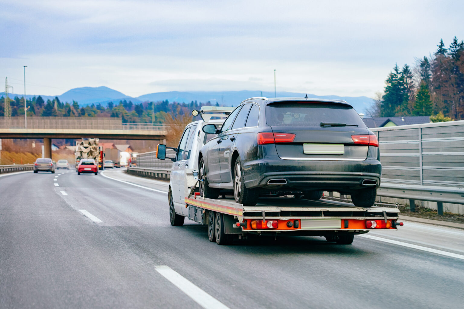 Tow truck with car on warranty in road. Trailer and crash auto delivery. Vehicles hauler on driveway. European transport logistics. Heavy haul trailer with driver on highway.