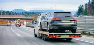 Tow truck with car on warranty in road. Trailer and crash auto delivery. Vehicles hauler on driveway. European transport logistics. Heavy haul trailer with driver on highway.