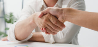 Multiracial group of young creative people in smart casual wear discussing business shaking hands together and smiling while sitting in modern office. Partner cooperation, coworker teamwork concept.