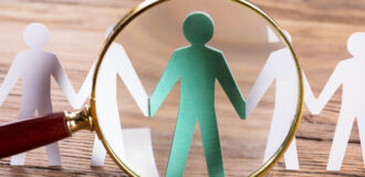 Magnifying Glass On Cut-out Figures On Wooden Desk